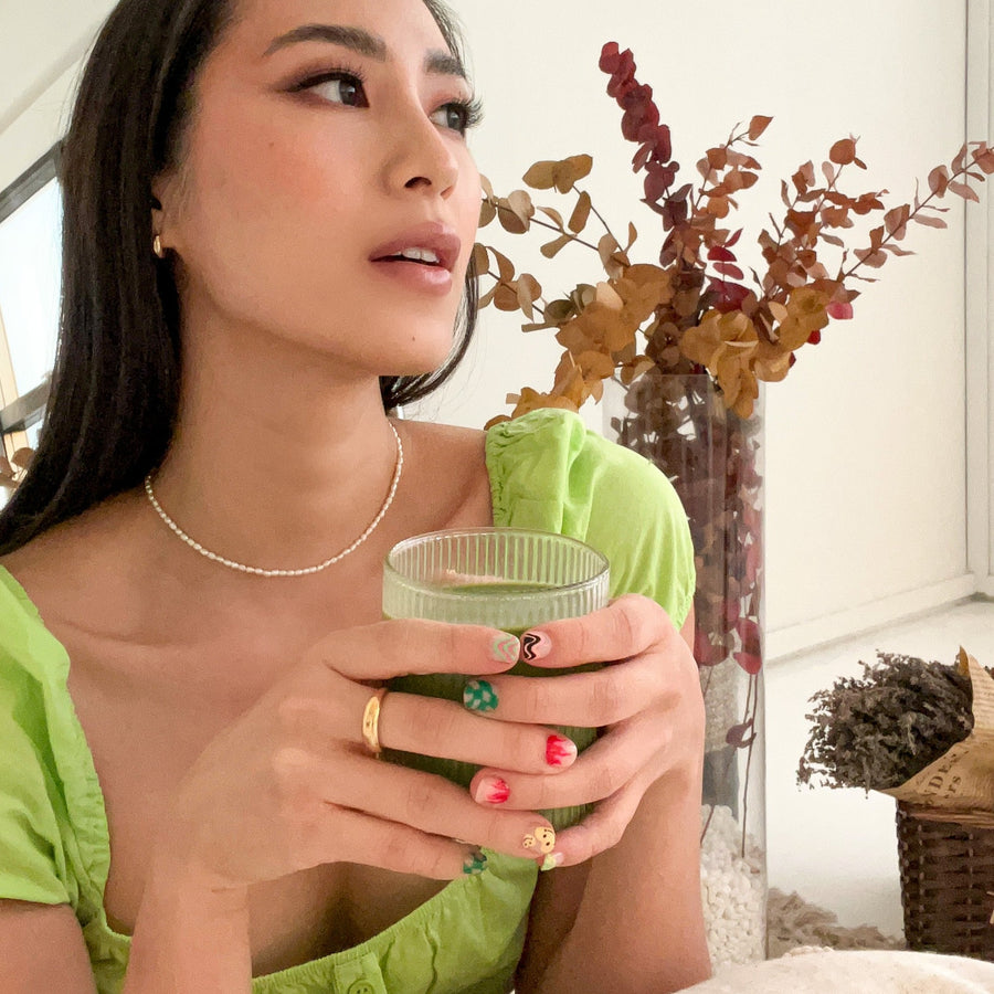 girl holding matcha drink wearing gold dainty dome ring, freshwater seed pearl necklace and micro crescent moon hoop earrings