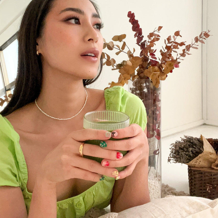 girl holding a matcha drink wearing the freshwater seed pearl necklace, gold dainty dome ring and 18ct gold vermeil crescent moon hoop earrings